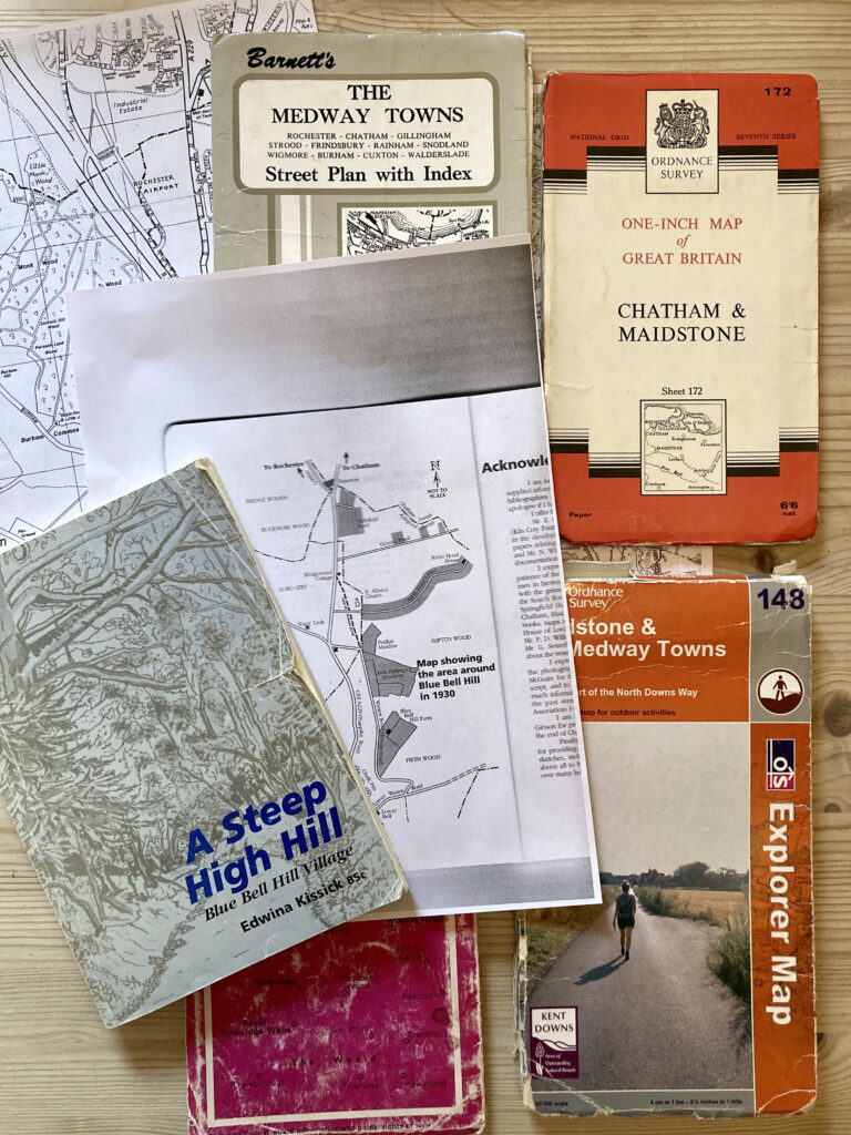 A collection of old Ordnance Survey maps of the area on a table, alongside a copy of the book, 'A Steep High Hill' by Edwina Kissick and a photocopy of a map showing the area round Blue Bill in 1930. 