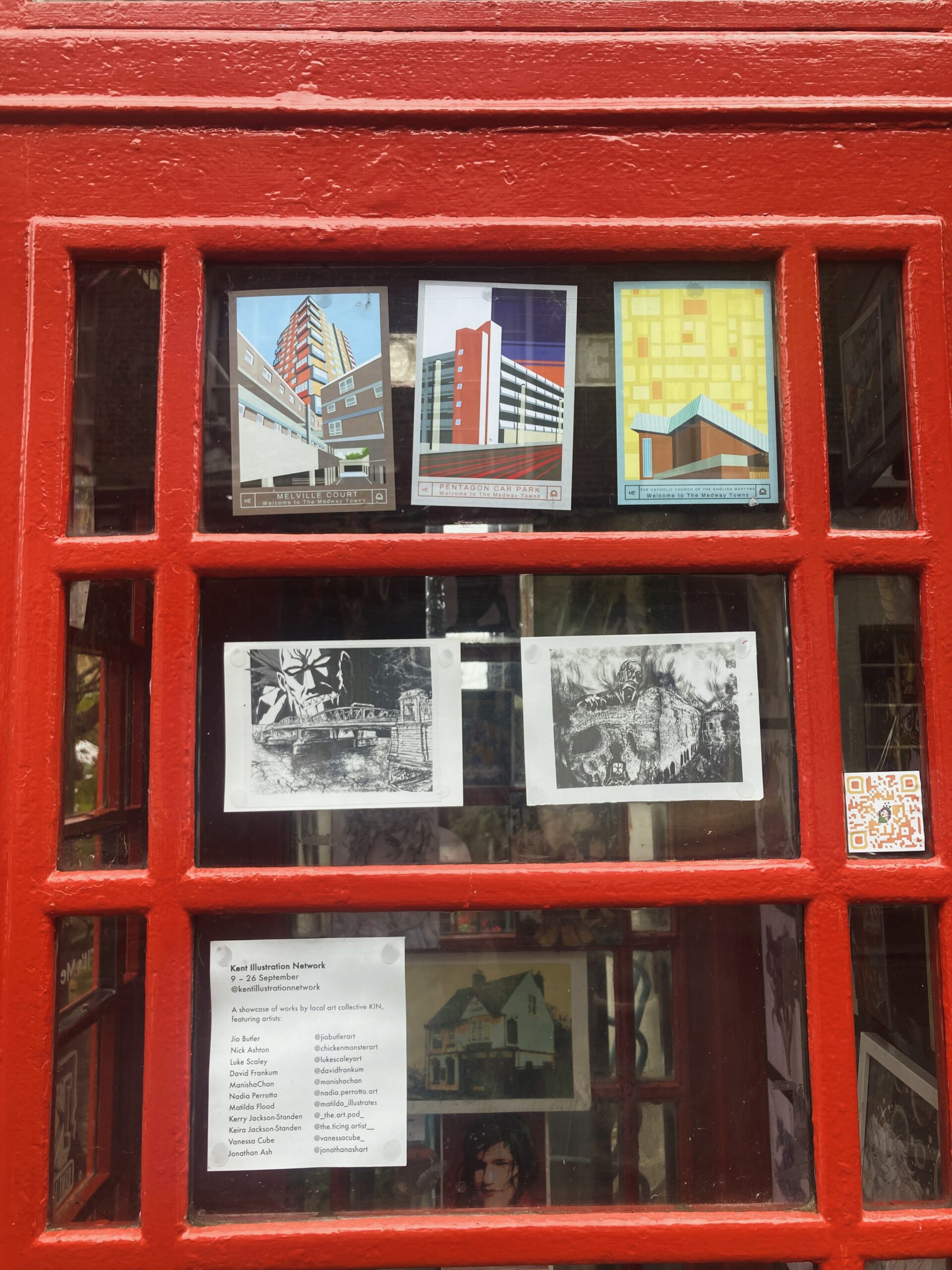 Close of up of a red telephone box with modern art postcards of Medway on the door. The postcards show local buildings including the Pentagon Centre, Melville Court and the Catholic Church of the English Martyrs. 