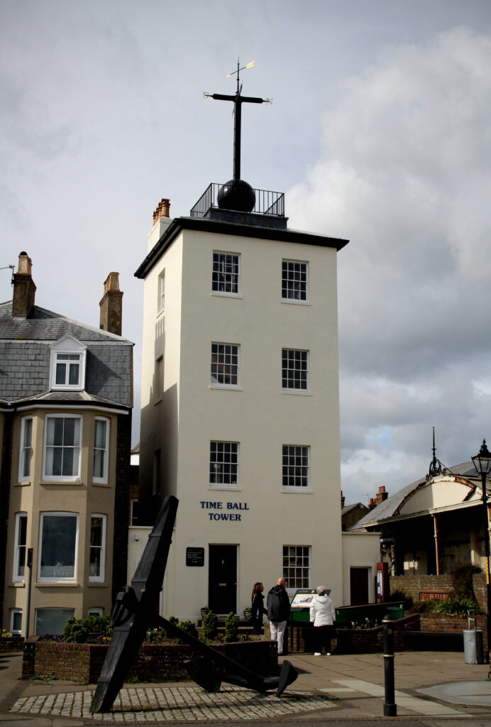 Exterior of the Timeball Tower in Deal. It is a tall, slim, white building with a black iron timeball on the roof.