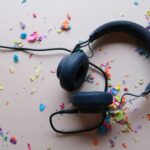 A set of black over-ear headphones on a pale white background, surrounded by multi-coloured confetti.