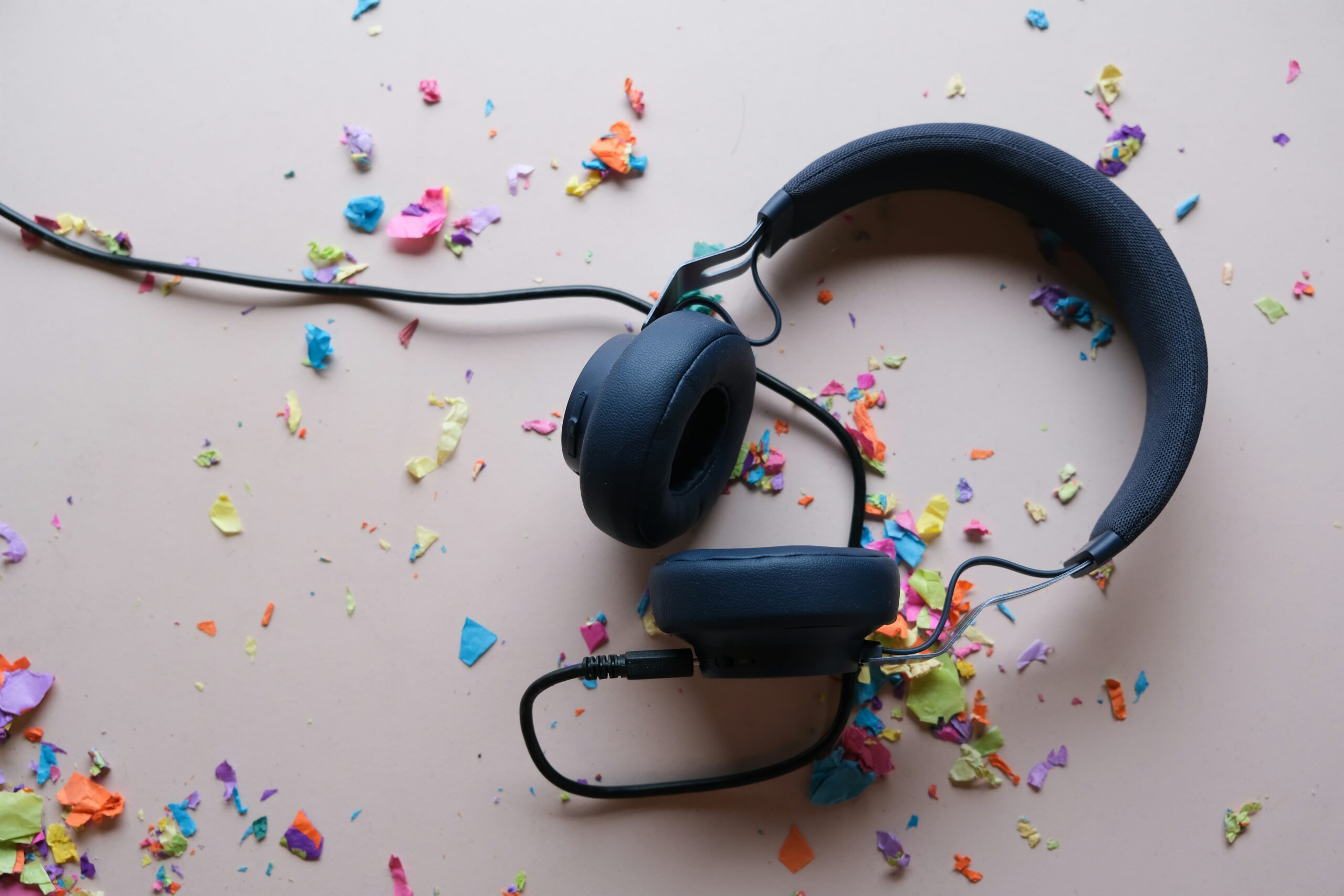 A set of black over-ear headphones on a pale white background, surrounded by multi-coloured confetti.