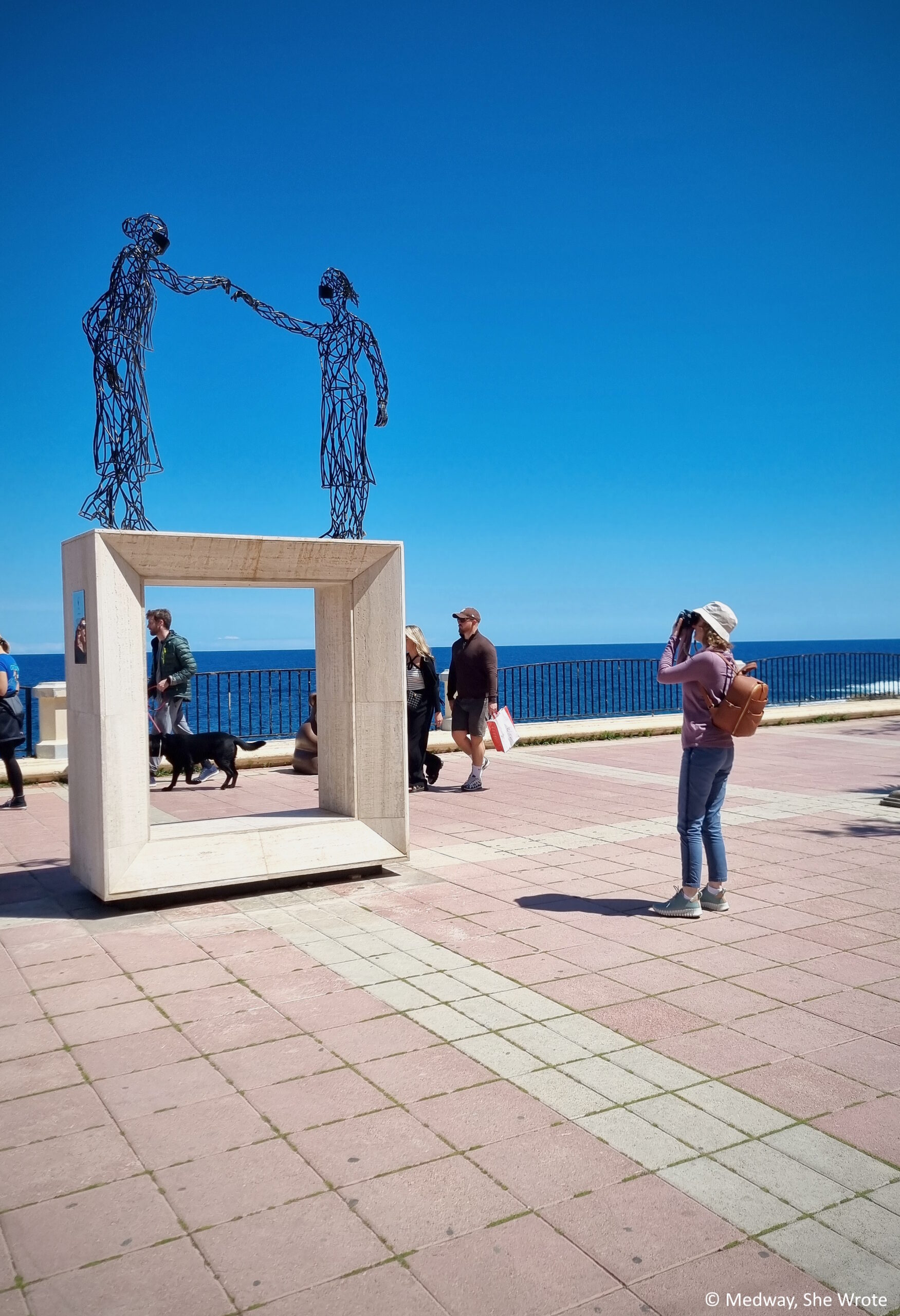 A woman taking a photo of the Covid memorial on the seafront in Sliema on a clear sunny day.