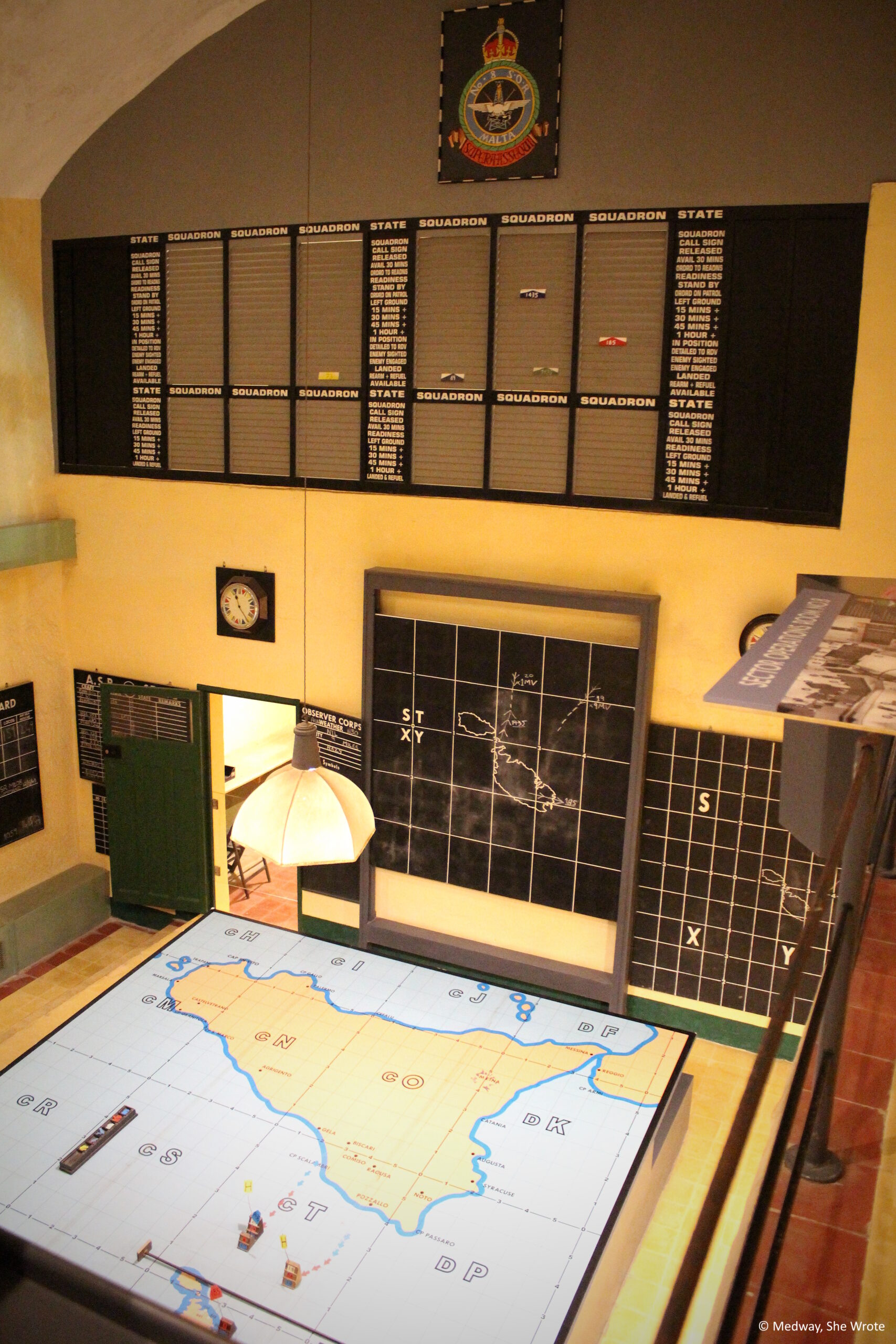 A view from above part of the operations rooms at Lascaris War Rooms. There is a table with a map of Malta on it, and other military charts and plans around the room.