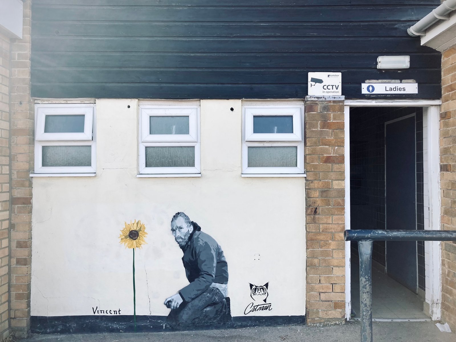 'Vincent' by Catman on the outside of the ladies' loo near Whitstable harbour. Van Gogh is kneeling on the ground next to a single, tall sunflower. Catman's logo is on the mural.