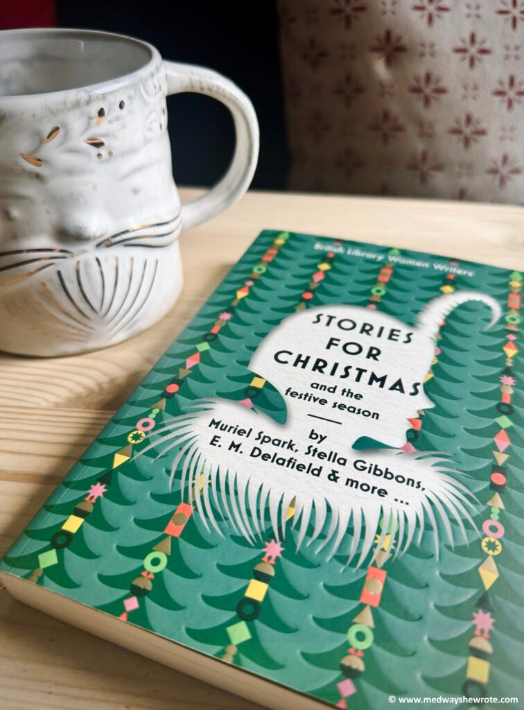 A paperback copy of 'Stories for Christmas and the Festive Season' on a table alongside a large white mug shaped like Santa's face.