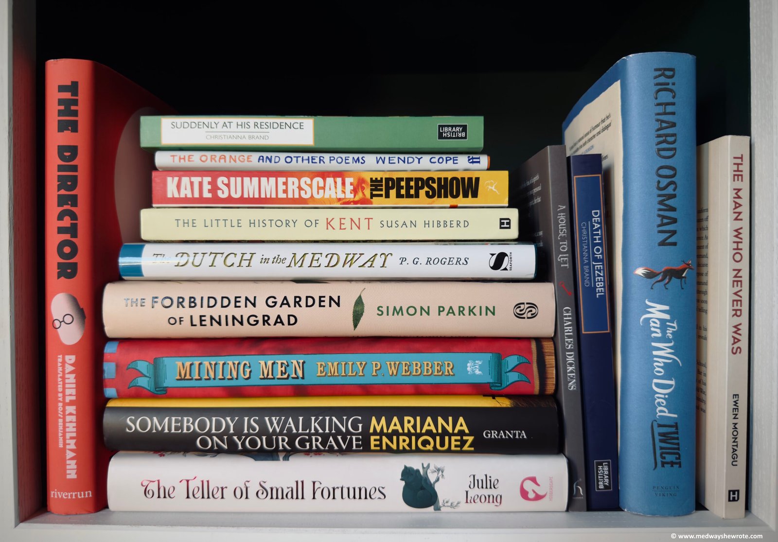 A collection of books on a shelf, arranged vertically and horizontally. There are paperbacks and hardbacks in a range of colours and designs.