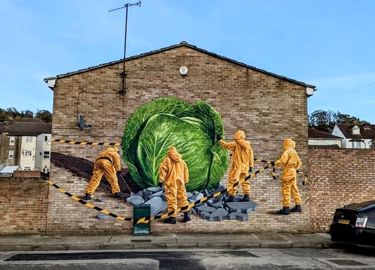 The Cabbage mural on Henry Street. A giant green cabbage is being inspected by four people in yellow hazmat suits.