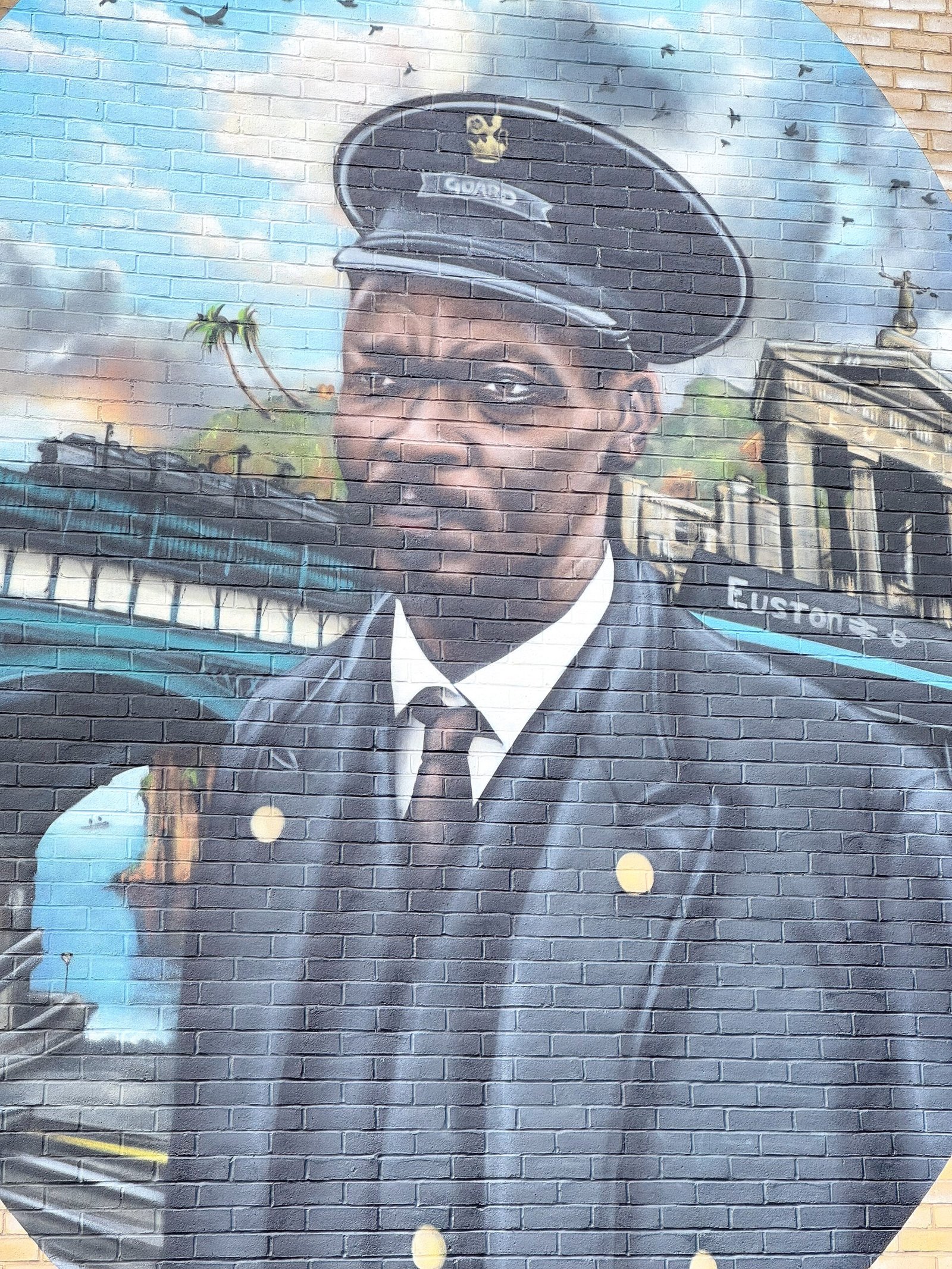 Close of the mural of Asquith Xavier. Xavier is shown in his train guard uniform with a train crossing a bridge and a Euston station sign in the background.