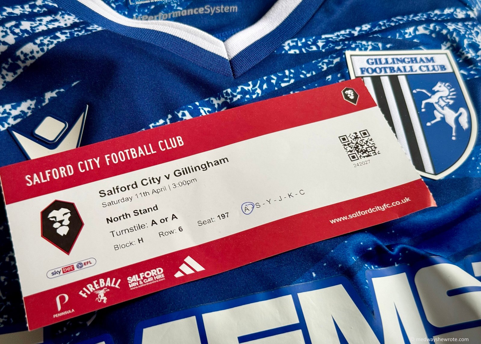 A match ticket for Salford City v Gillingham pictured on top of a Gillingham home football shirt.