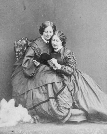 A black and white image of Georgina Hogarth and Mamie Dickens reading a book together. 