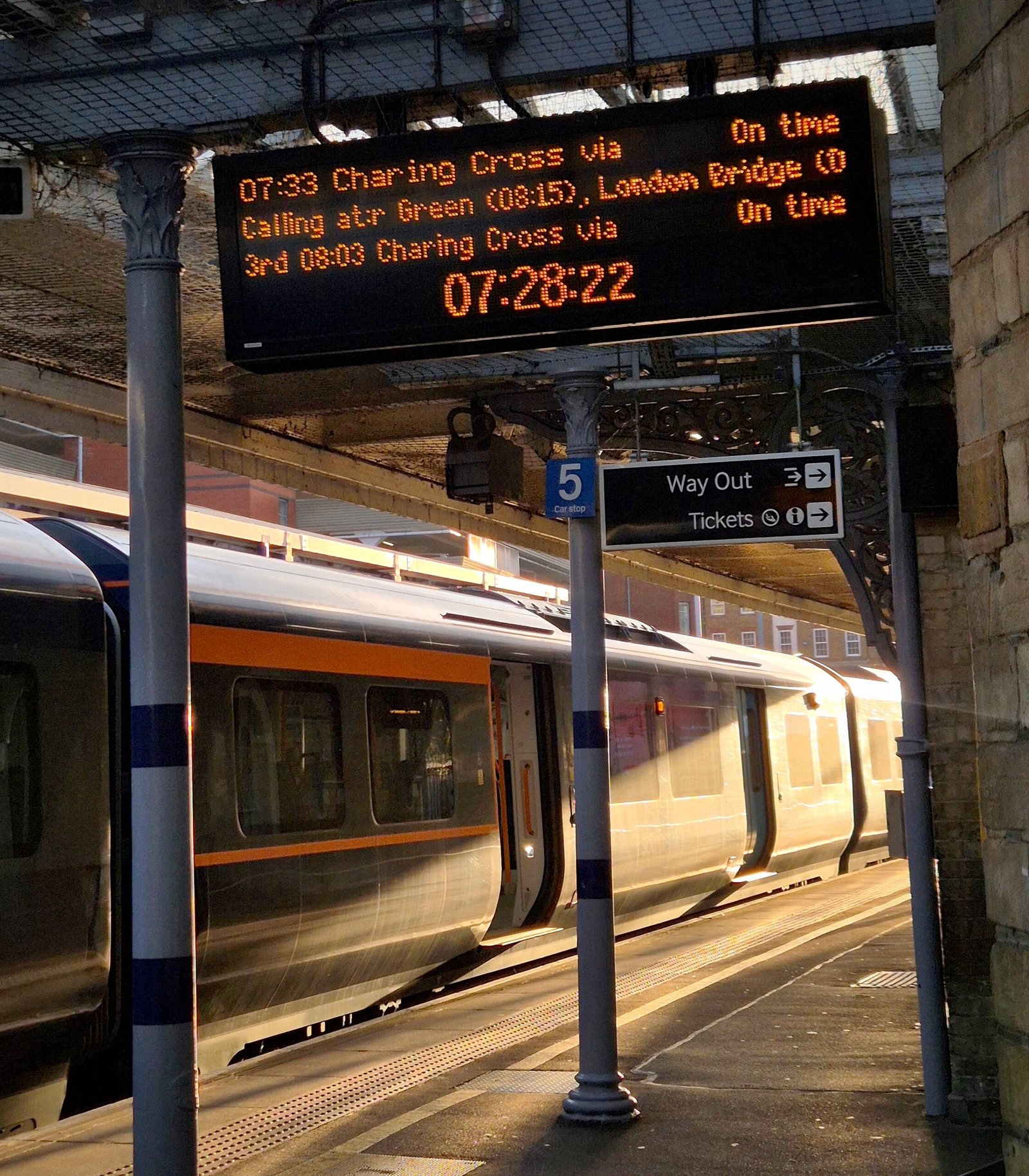 A departure board on a station platform showing the departure times for trains to London Charing Cross.